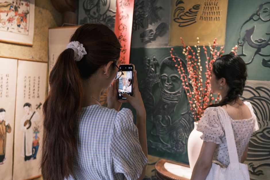 Two women admire and photograph artworks in a traditional cultural art gallery.