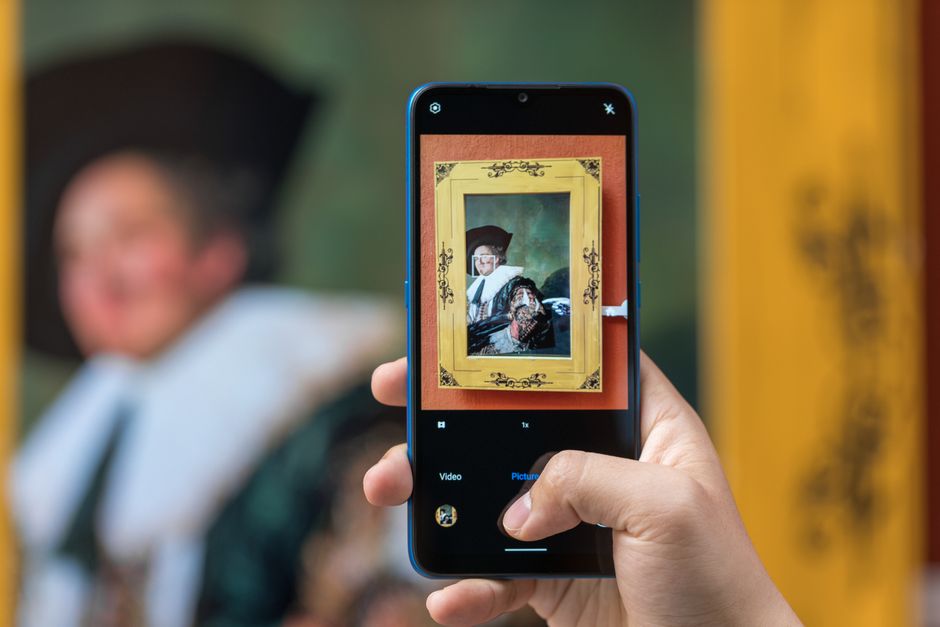 Close-up of a smartphone photographing an antique painting in a gallery setting.