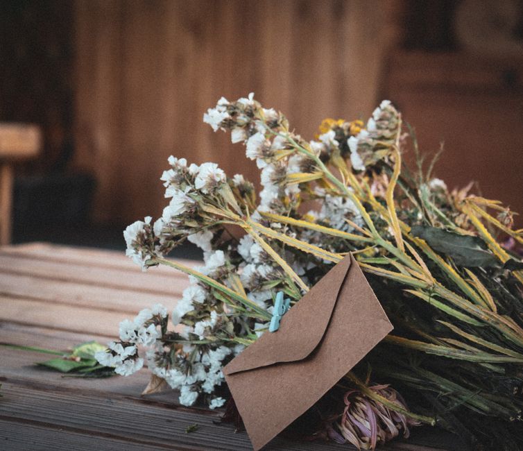 A bouquet of dried white flowers alongside a brown envelope on a wooden table.