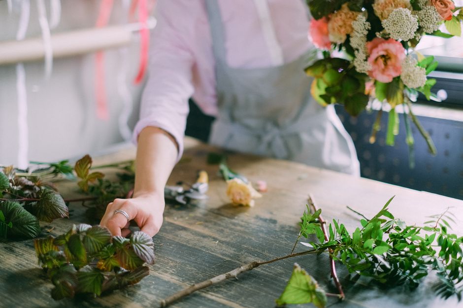 A florist in an apron arranging a beautiful bouquet of pink and white flowers indoors.